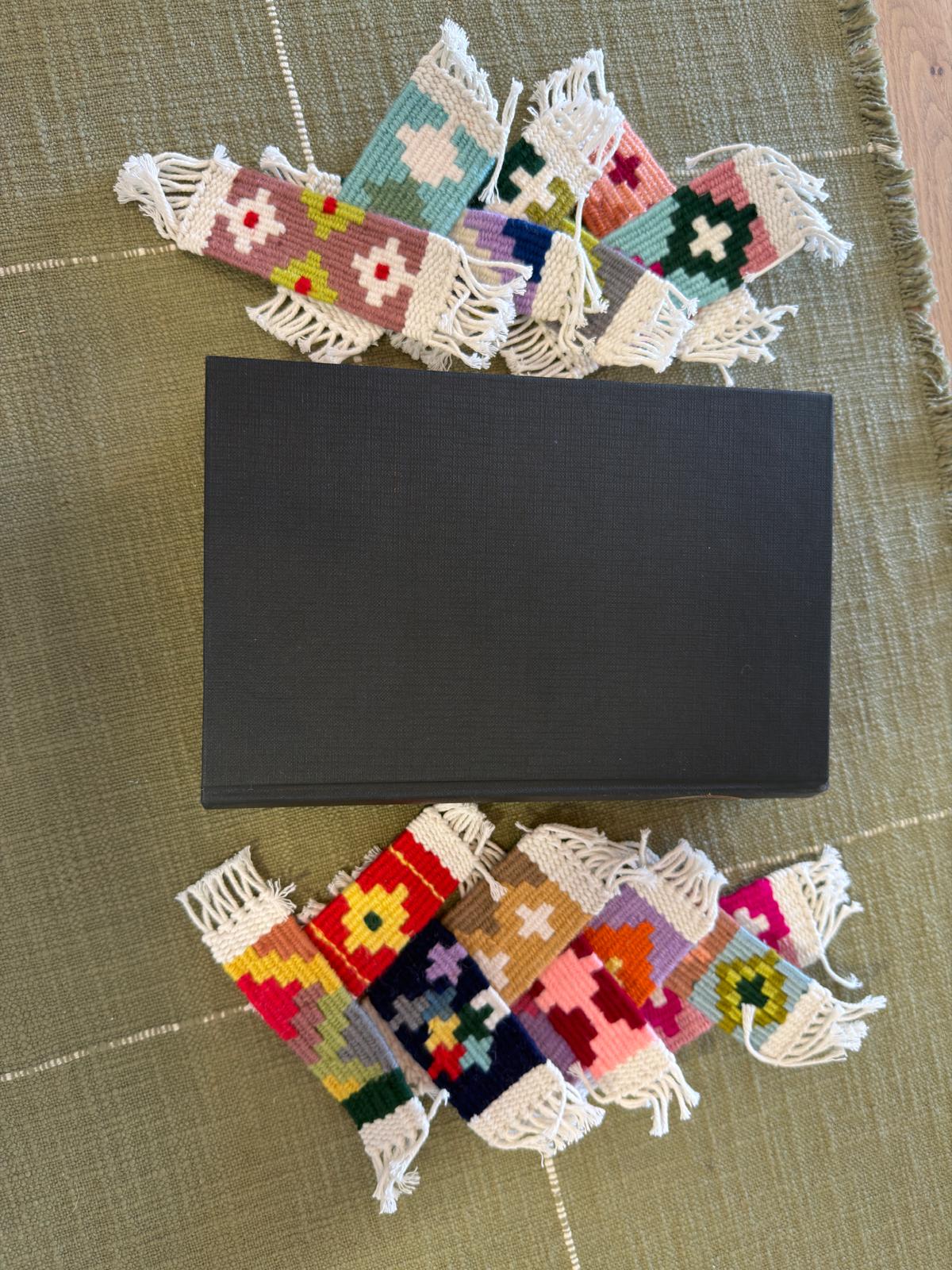 Colorful woven coasters with fringe on a black box on a textured surface