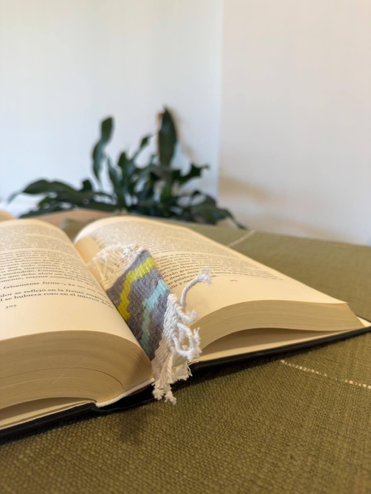 Open book with a colorful bookmark on a green surface, blurred plant in the background