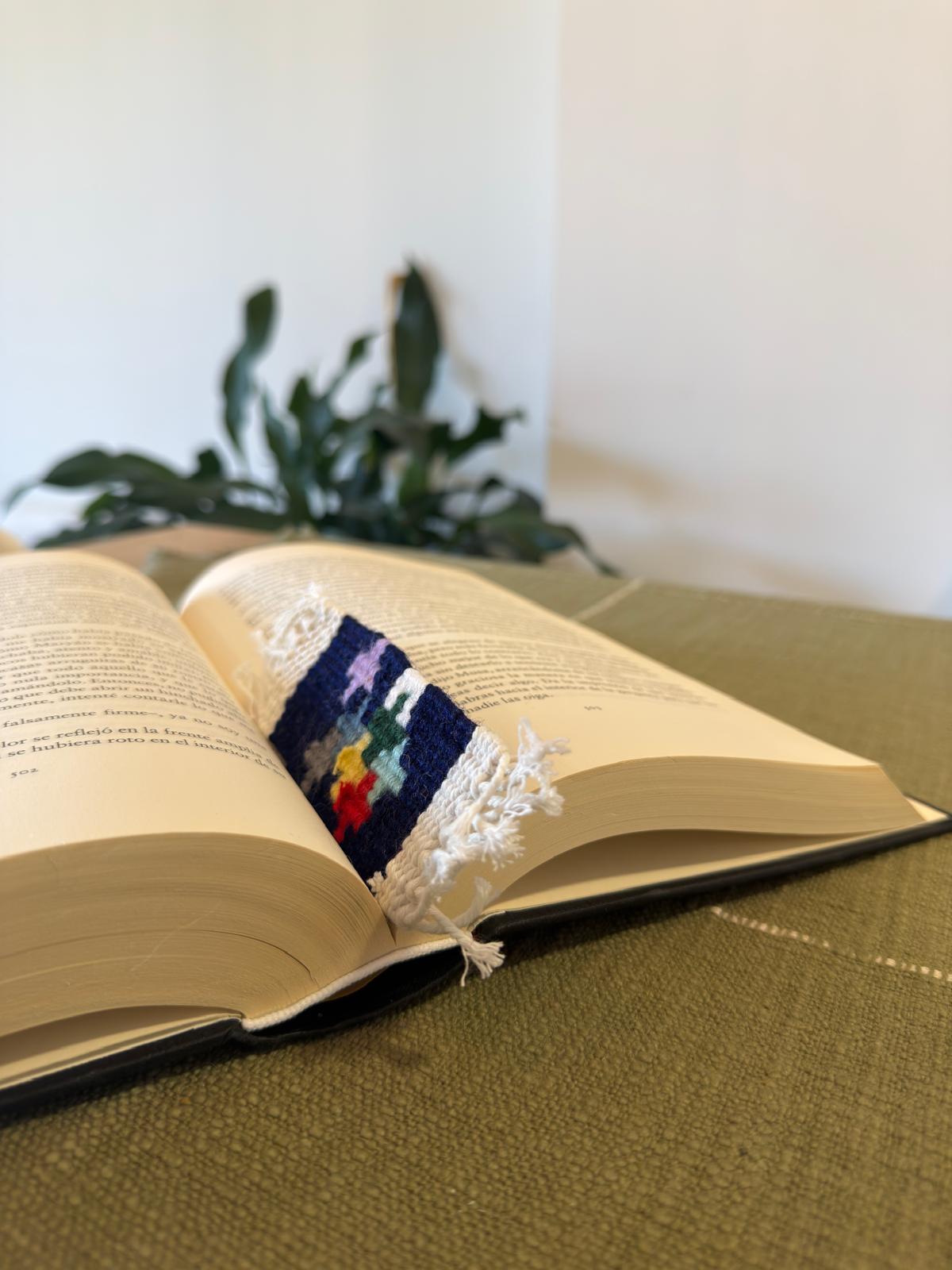 Open book with a decorative bookmark on a green surface, plant in the background