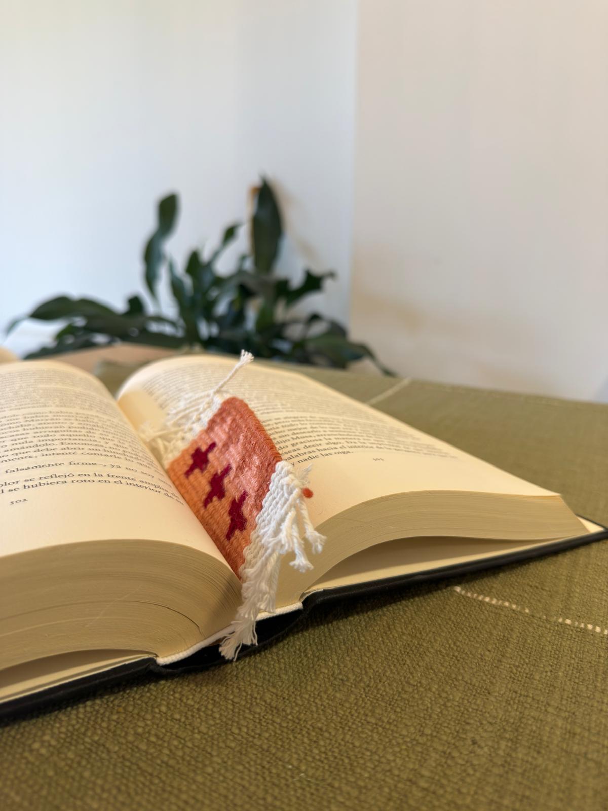 Open book with a decorative bookmark on a green surface, plant in the background