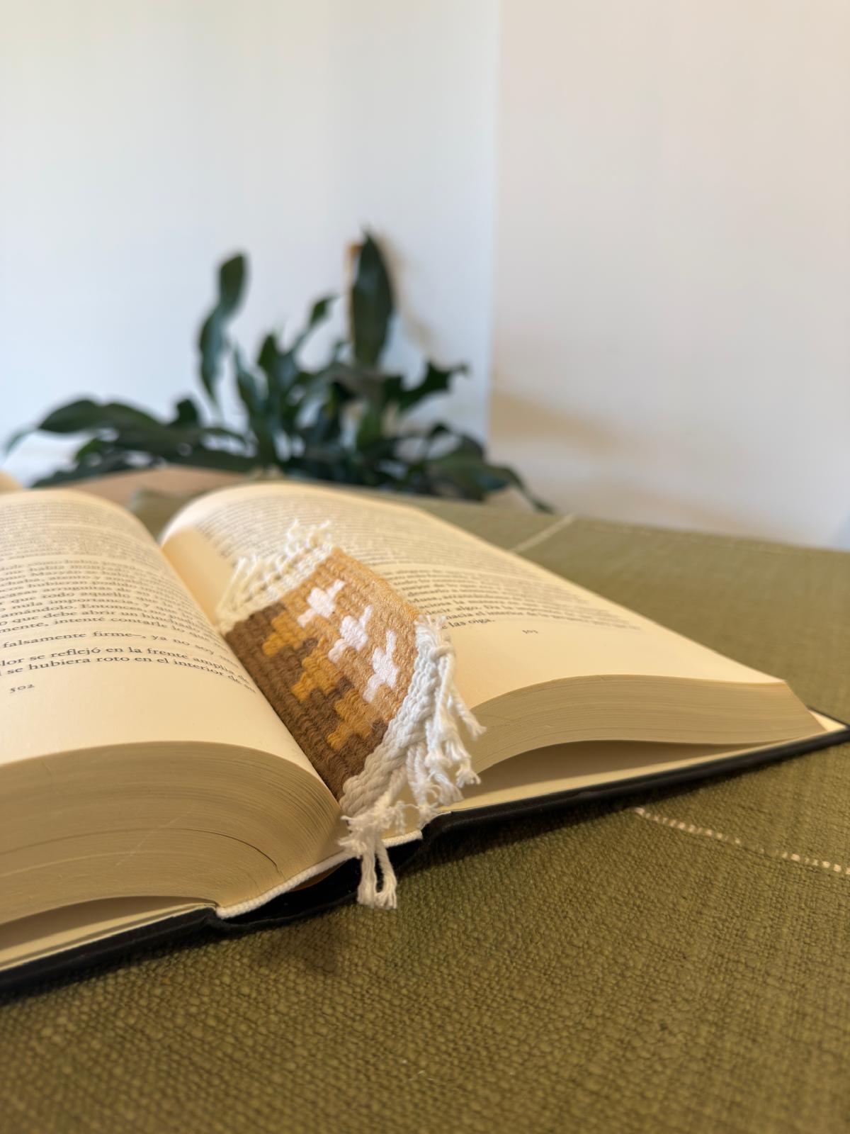 Open book with a decorative bookmark on a green surface, blurred plant in the background