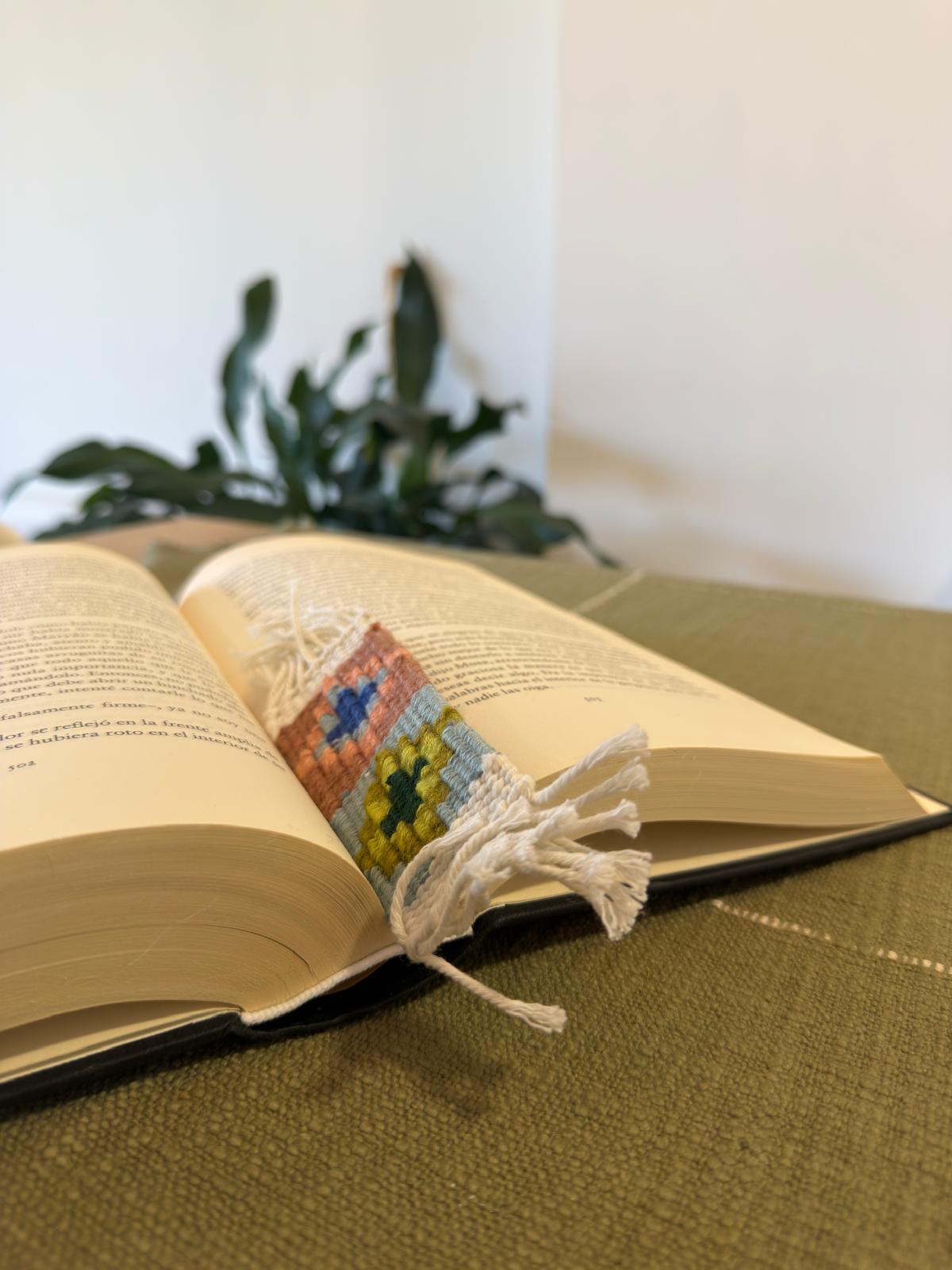 Open book with a colorful woven bookmark on a textured surface.