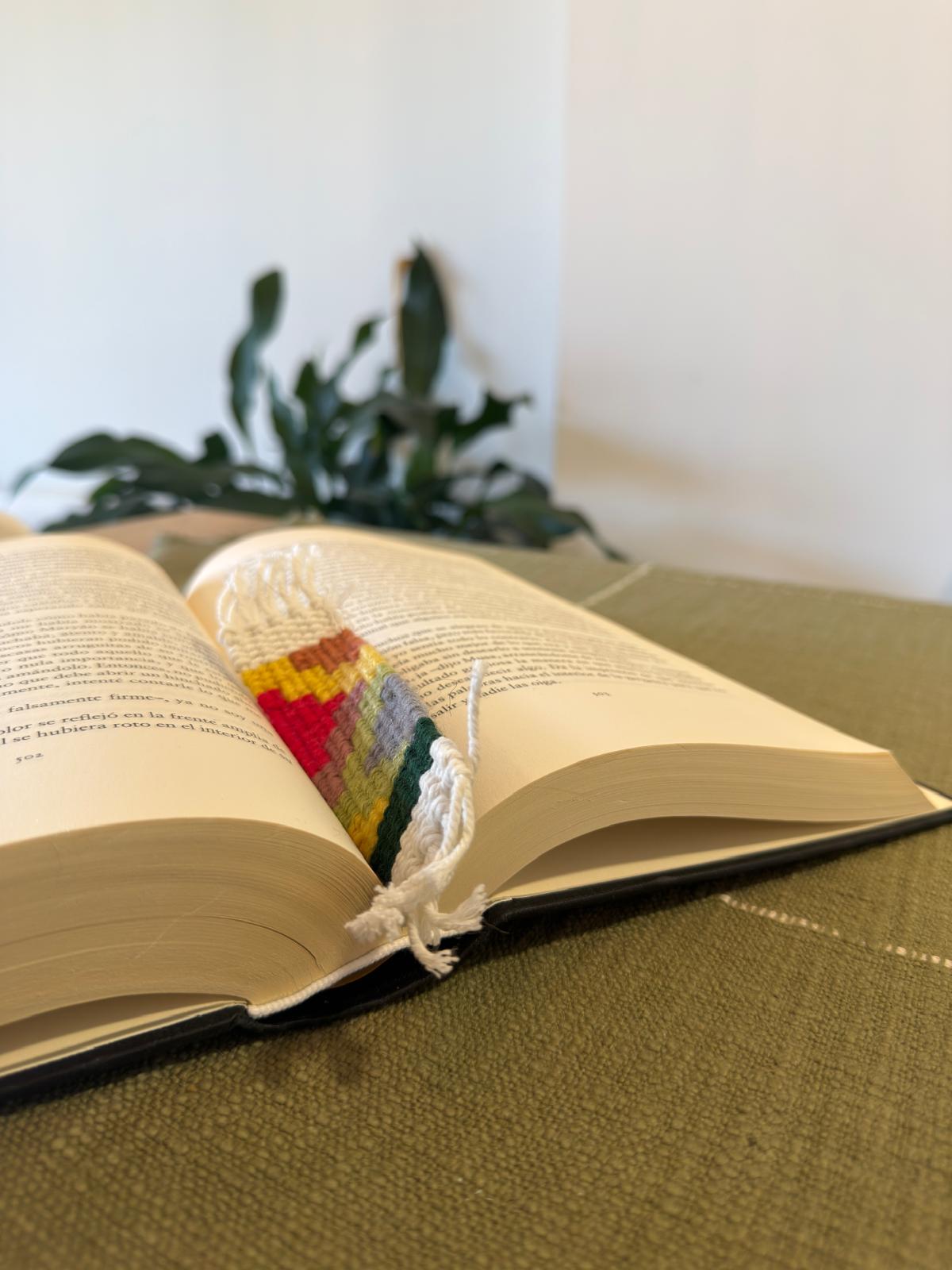 Open book with a colorful woven object on a green surface