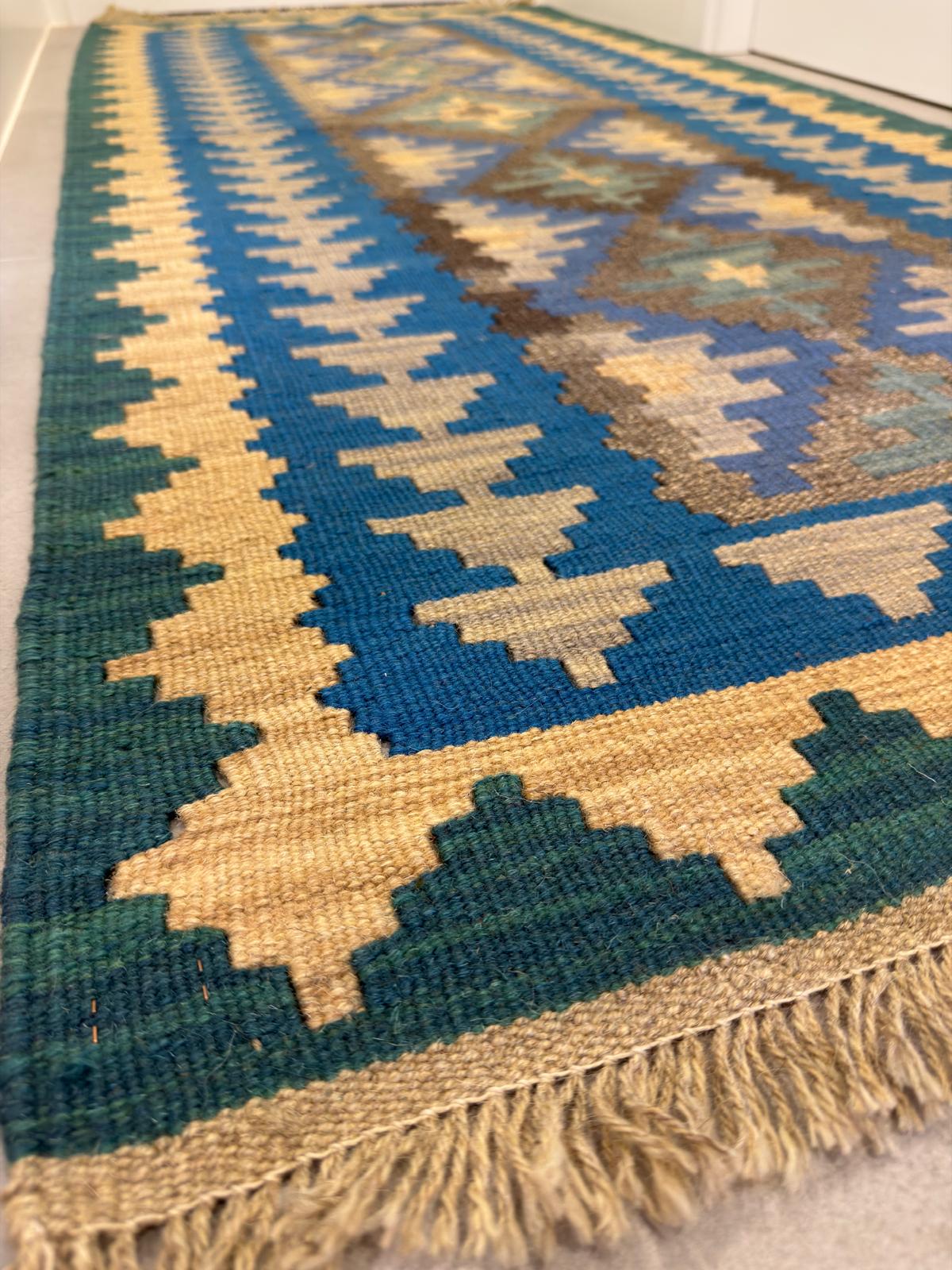 Woven rug with geometric pattern in blue, green, and beige on a plain background