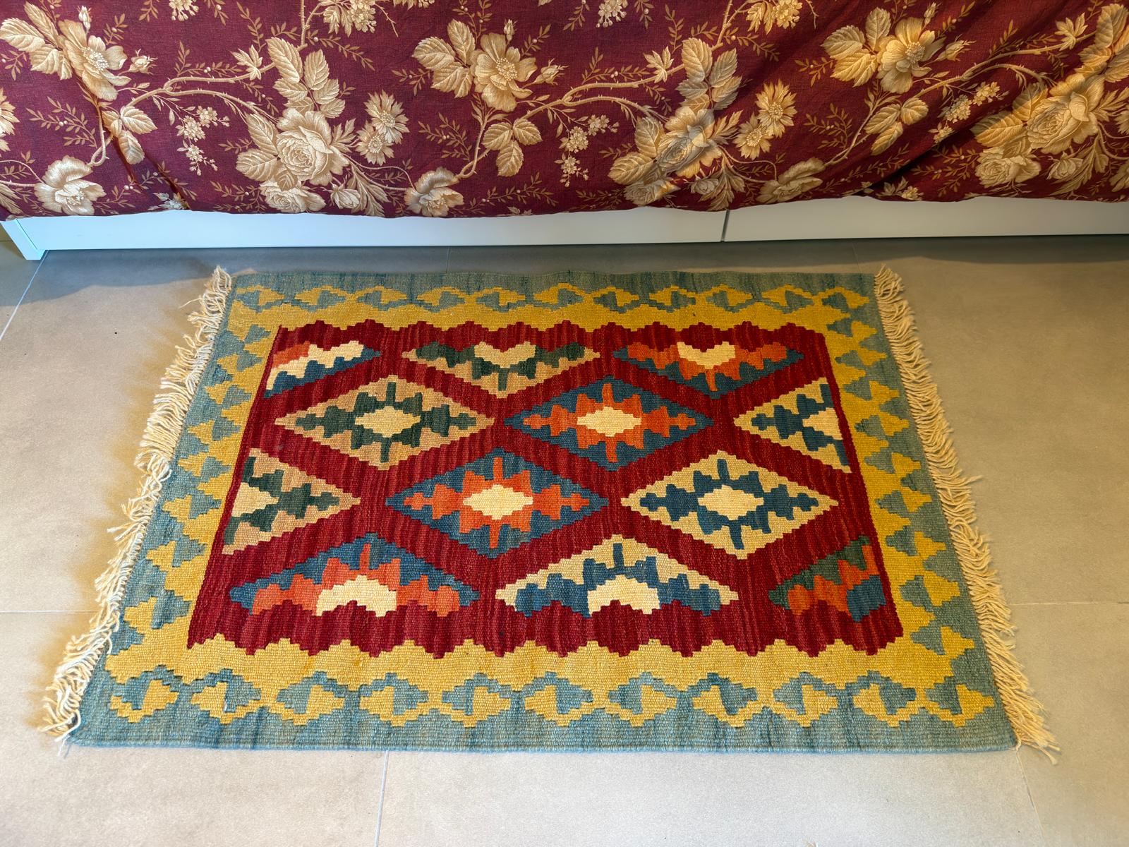 Decorative rug with geometric pattern on a beige floor, with a floral-patterned fabric in the background.