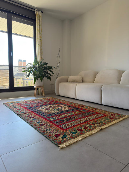 Living room with a colorful patterned rug, beige sofa, and a plant near a window.