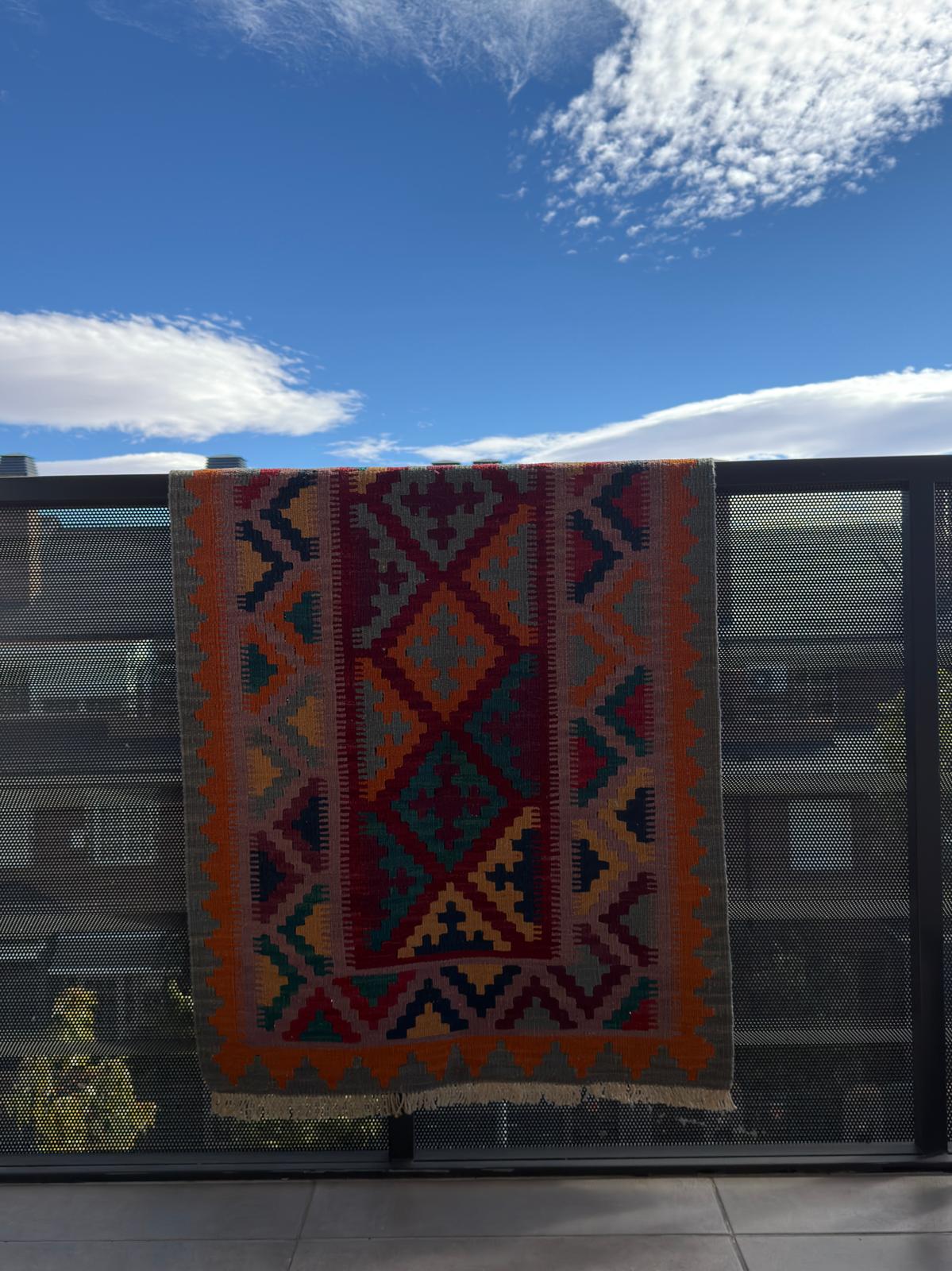 Colorful patterned rug on a glass door with a blue sky and clouds in the background
