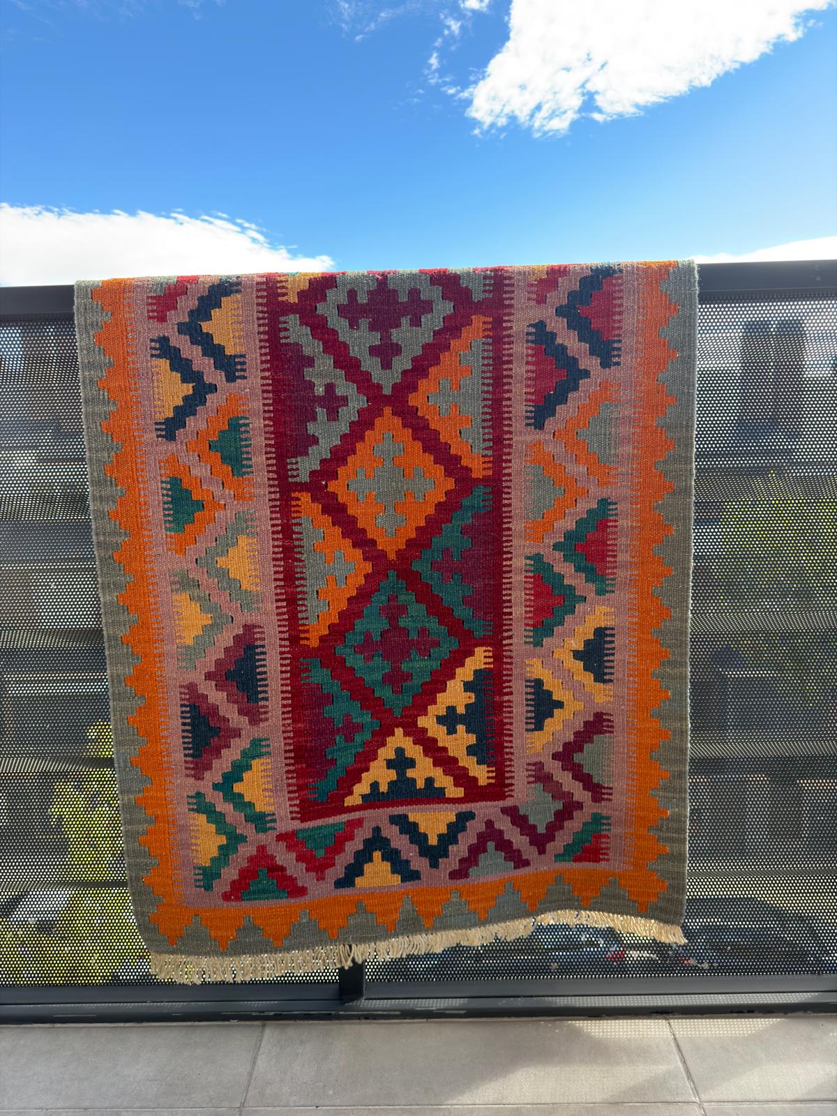 Colorful patterned blanket draped over a railing with a blue sky and clouds in the background.