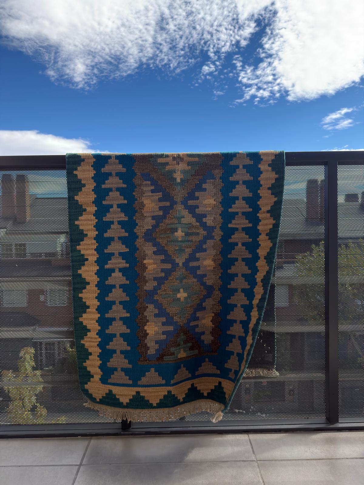 Textile with geometric pattern draped over a railing against a blue sky.