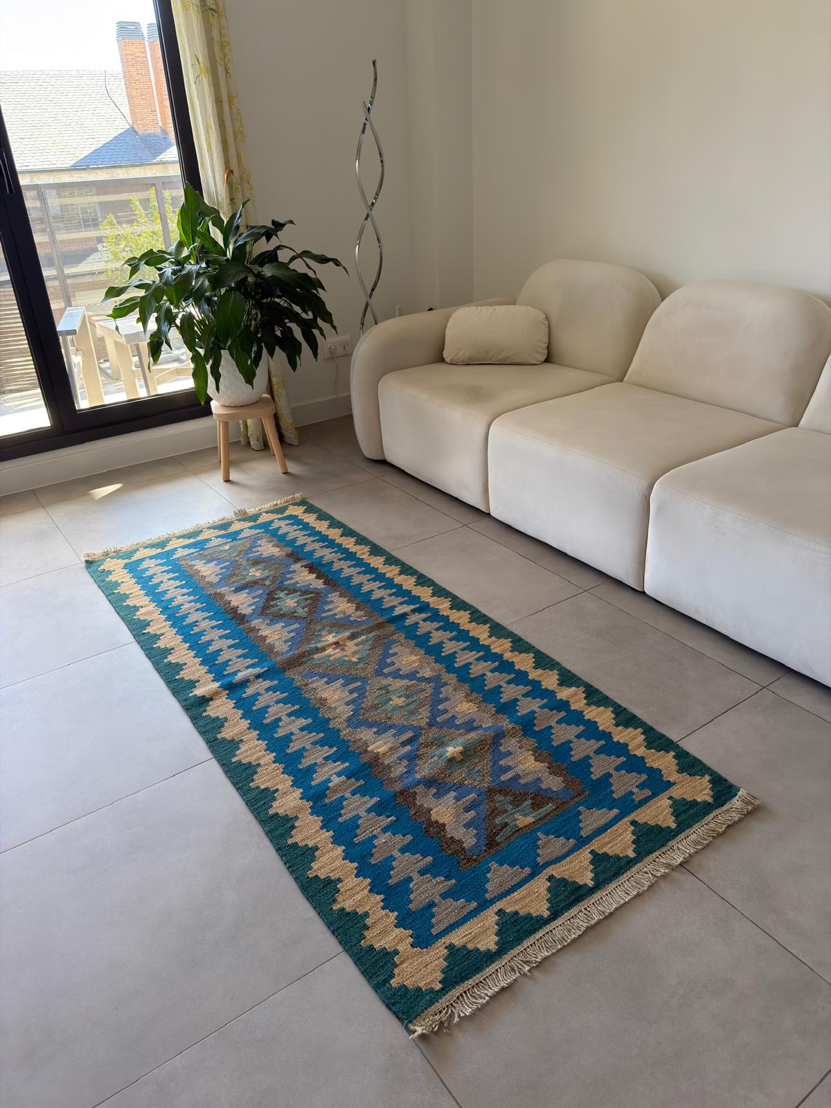 Blue and beige patterned rug on a tiled floor in a living room with a beige sofa and plant.