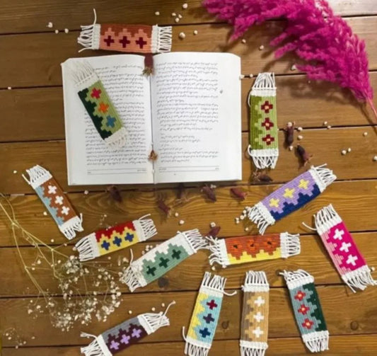 Colorful woven bookmarks on an open book with decorative elements on a wooden surface.
