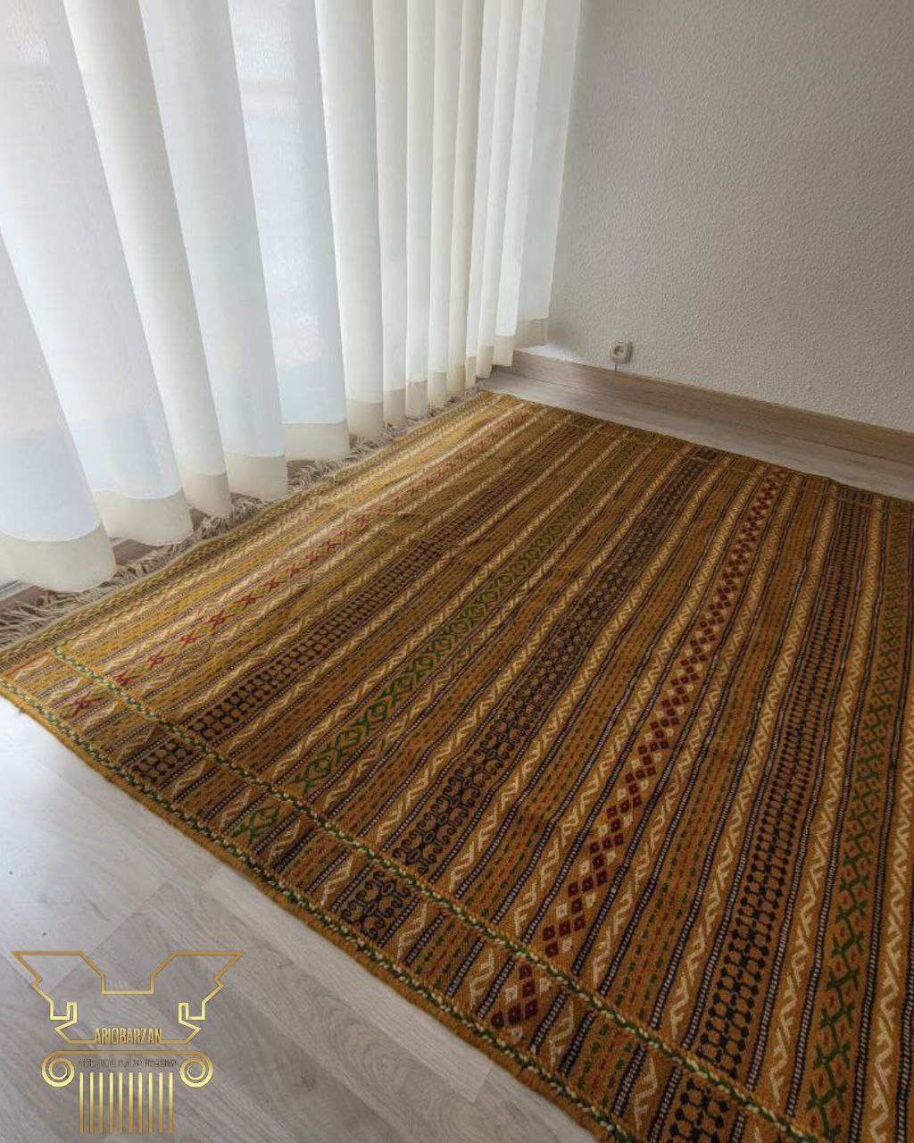 Patterned rug on a wooden floor with white curtains in the background
