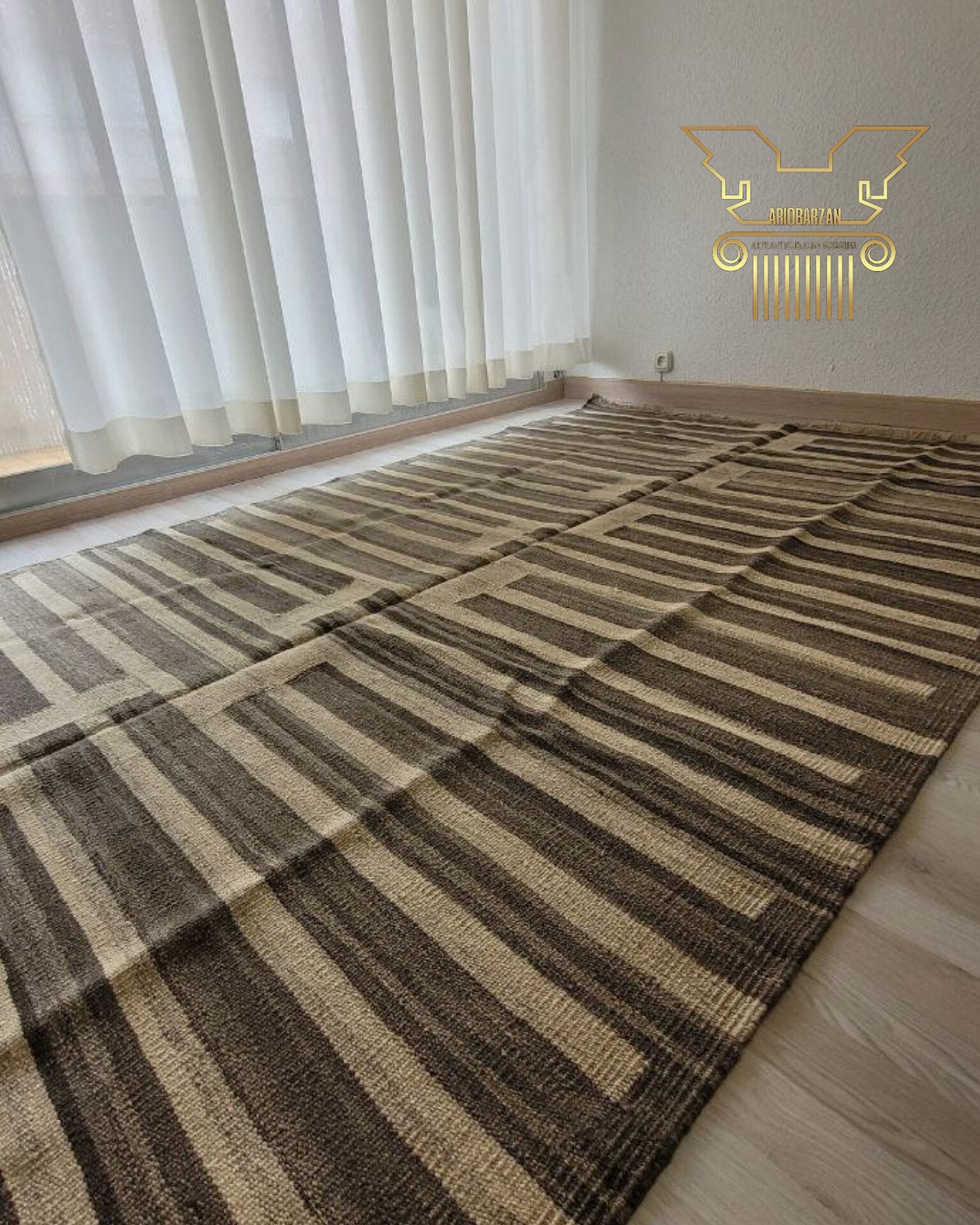 Brown and beige checkered rug on a wooden floor with white curtains in the background.